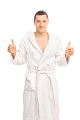 Happy young man in a white bathrobe giving two thumbs up isolate
