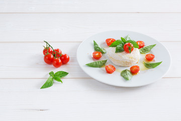 a round piece of cheese with basil and cherry tomatoes on a white plate