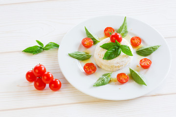 round piece of cheese with basil and cherry tomatoes on a white plate