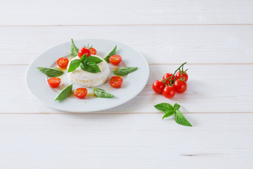 round piece of cheese with basil and cherry tomatoes on a white plate