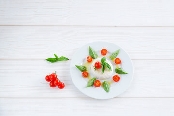 round piece of cheese with basil and cherry tomatoes on a white plate