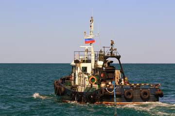 the old sea tug with a Russian national flag on the mast pulls the tow rope