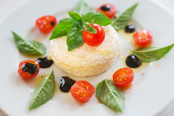 Fototapeta na wymiar round piece of cheese with basil and cherry tomatoes on a white plate