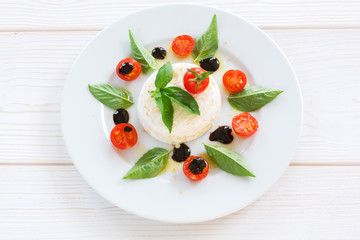 round piece of cheese with basil and cherry tomatoes on a white plate