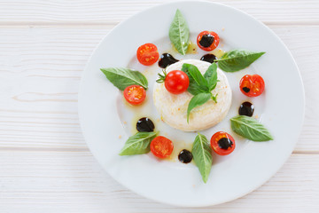 round piece of cheese with basil and cherry tomatoes on a white plate