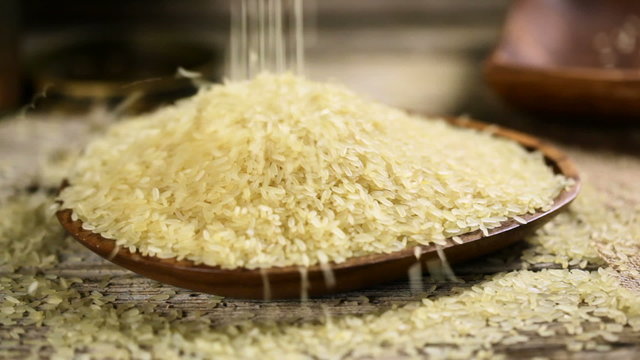 Rice grains falling into a wooden bowl