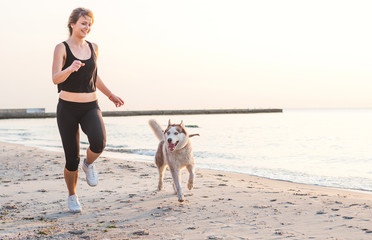 young caucasian female playing with siberian husky dog on beach during sunrise