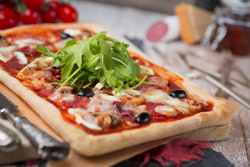 Homemade rectangular pizza on a rustic table with ingredients