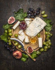 cheese plate with gorgonzola and Camembert cheese with Knife for cheese  white and dark grapes, honey and jam on a wooden cutting board on a dark rustic background top view close up - obrazy, fototapety, plakaty