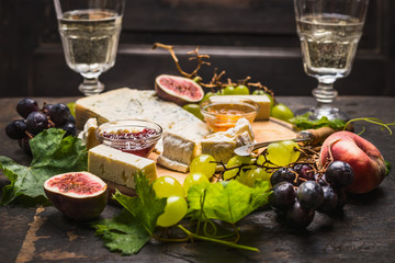 cheese plate with white and dark grapes on a branch Peaches glasses on wooden rustic background