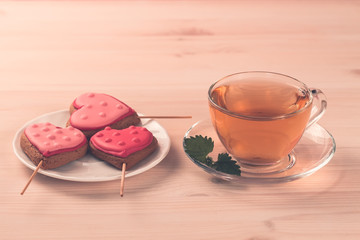 delicious fresh cookies in the shape of a heart on a white plate on wooden background. Cup of green tea. Breakfast