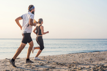 Running people - woman and man athlete runners jogging on beach. Fit young fitness couple...