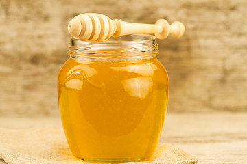 glass jar of honey with drizzler on wooden background