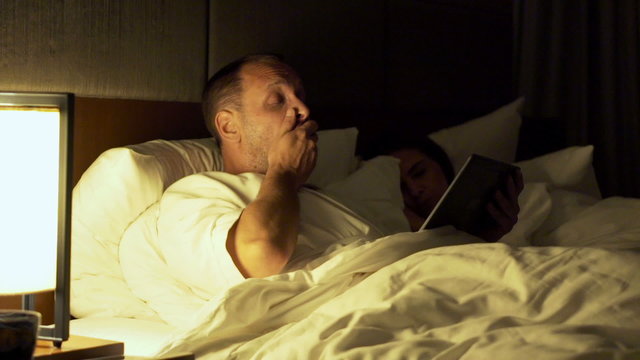 Couple in bed at night, man using tablet computer and going to sleep