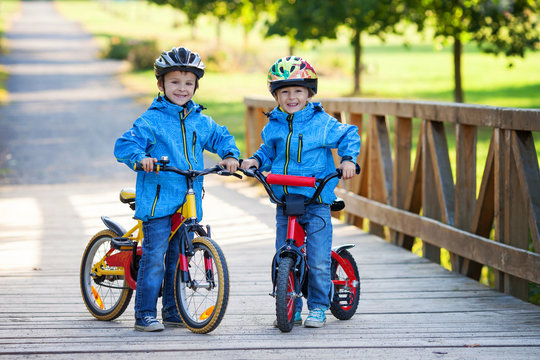 Two Cute Boys, Siblings Children, Having Fun On Bikes In The Par