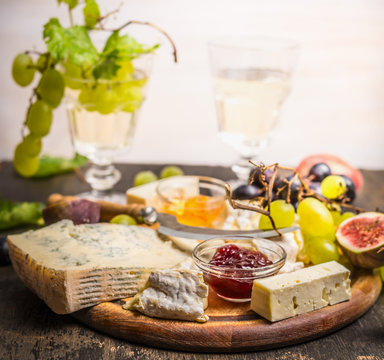 cheese plate with Gorgonzola and Camembert with honey and jam dark and bright grapes glass of wine grapes on a branch inside on dark wooden background close up