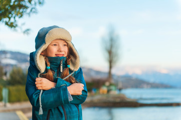 Outdoor portrait of adorable little girl on a nice winter evening, resting by the lake at sunset