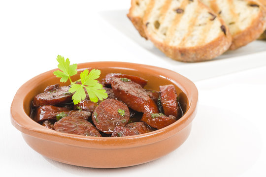 Chorizo al Vino (Spicy sausage cooked in red wine). Traditional Spanish tapas dish. Other tapas dishes on background.

