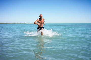 Bald middle-aged man running fast on the lake with a naked torso