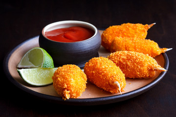 Rustic plate of fried breaded surimi crab claws with bowl of tom