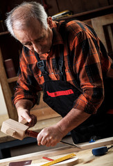 Fototapeta na wymiar Closeup of a senior carpenter working with a hammer, chisel and wood carving tools.