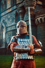 Medieval knight with the sword on the ancient castle background