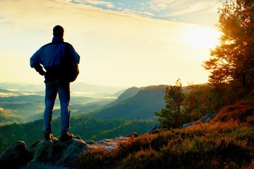 Silhouette of tourist with backpack. Sunny spring daybreak in rocky mountains. Hiker with sporty backpack stand on rocky view point above misty valley.