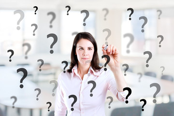 Young business woman writing question mark. Office background.