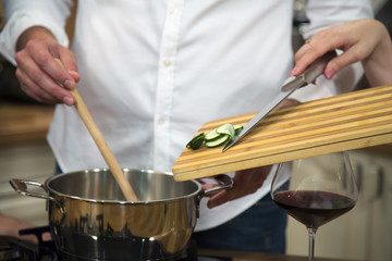 Couple cooking together and adding sliced vegetables to cooking