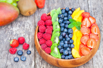 Fresh colorful fruits and berries in wooden bowl on rustic table