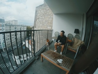 man is sitting on balcony with book in company of his dog