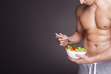 Athletic man holding a bowl of fresh salad on grey background