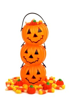 Stack of Halloween Jack o Lantern candy holders with pile of candy pumpkins and candy corn over white