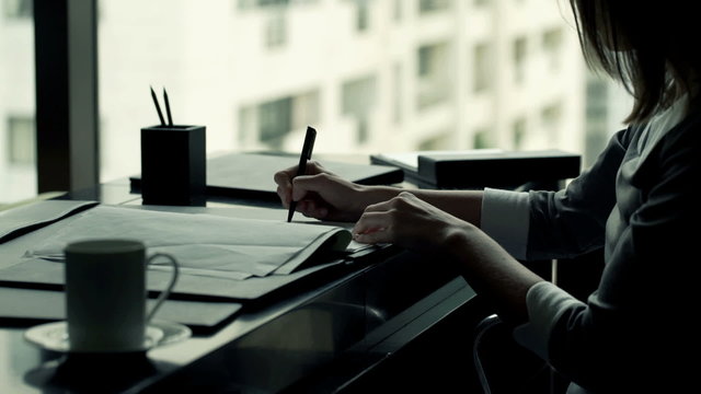 Businesswoman writing notes in documents sitting by desk in office