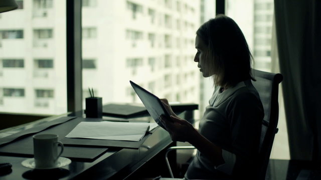 Young businesswoman working with documents and tablet computer by desk in office
