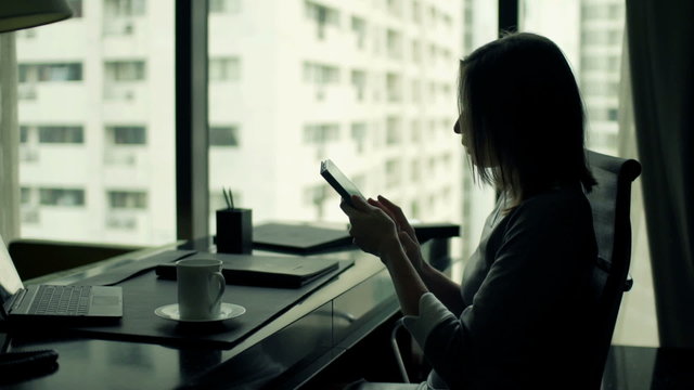 Young businesswoman using smartphone while sitting by desk in office