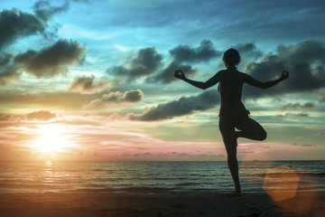 Fototapeta premium Silhouette of young women standing at yoga pose on the beach during an amazing surreal sunset.