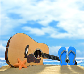 Acoustic guitar and flip flops on the sandy beach in summer with blue sea and sky