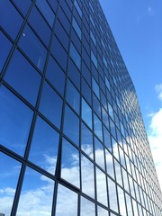 Fototapeta na wymiar grattacielo di vetro che riflette cielo azzurro e nuvole