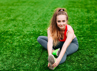 Fototapeta premium Young fitness girl sitting on green grass .