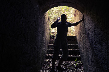 Young man with flashlight enters dark stone tunnel