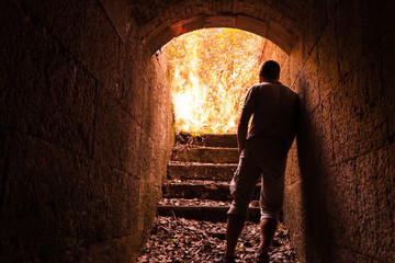 Young man stands in dark stone tunnel with big fire