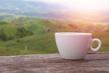 White coffee cup on wooden table with mountains view
