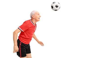 Zelfklevend Fotobehang Senior in a red jersey heading a football © Ljupco Smokovski