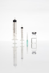 syringe needle and vaccine set up on white background with reflection