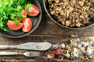 On old wooden table, are fried mushrooms with butter and tomatoes