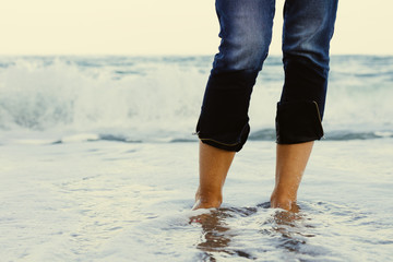 Female legs in jeans standing in the sea water on the background