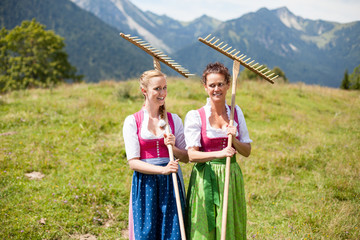 Zwei Bäuerinnen im Dirndl mit Rechen auf einer Almwiese