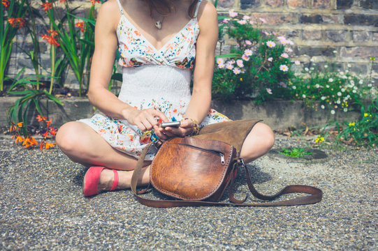 Woman sitting in street with phone and handbag