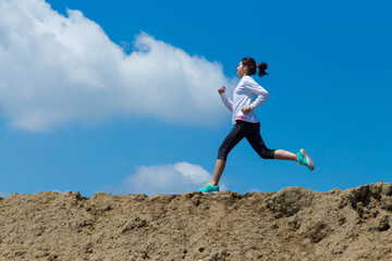 young woman running on mountain trail with blue sky background